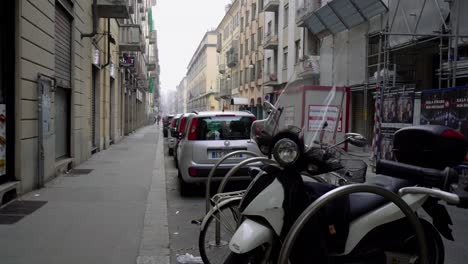 Paisaje-Urbano-Con-Vehículos-Estacionados,-Vespa-En-Primer-Plano.-Mano