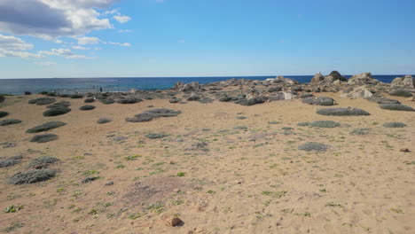 Eine-Sandige-Küstenregion-Mit-Spärlicher-Vegetation-An-Den-Königsgräbern-In-Paphos,-Zypern,-Unter-Blauem-Himmel