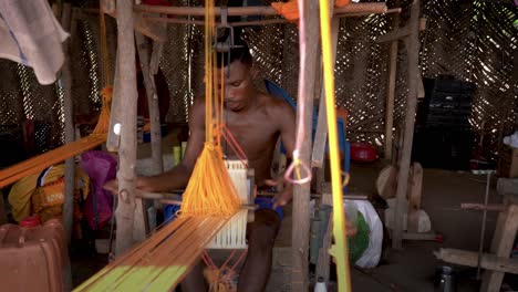 A-skilled-weaver-works-rapidly-on-a-wooden-loom-in-Ghana,-West-Africa-weaving-the-colorful-kente-cloth-for-traditional-African-clothing