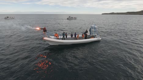 A-Sailor-Uses-Pyrotechnic-Flare-In-Distress-Signal-Testing-In-Patagonian-Sea-While-Other-Sailors-In-The-Boat-Are-Watching---orbital-Shot