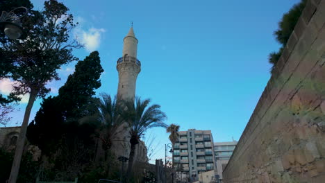 historic-mosque-with-a-tall-minaret-in-Pafos,-Cyprus,-with-palm-trees-and-modern-buildings-in-the-background