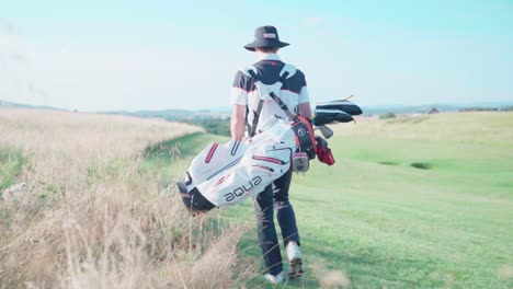 Golfer-on-golf-course-carrying-bag-with-clubs,-camera-tracks-though-field