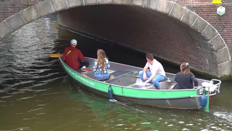 Four-people-on-a-turistic-boat-in-a-canal-in-Amsterda,-passing-under-a-bridge