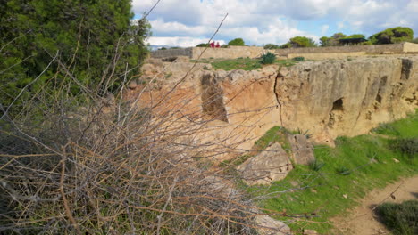 Una-Vista-Más-Cercana-Del-Sitio-Arqueológico-De-Las-Tumbas-De-Los-Reyes-En-Pafos,-Chipre,-Con-Terreno-Rocoso-Y-Estructuras-Antiguas.