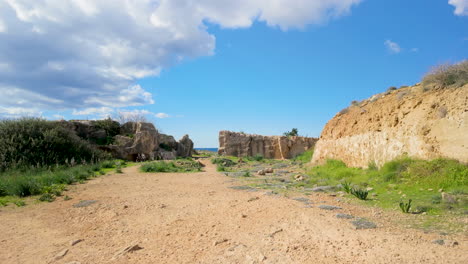 A-pathway-through-rocky-ruins-at-the-Tombs-of-the-Kings-in-Pafos,-Cyprus,-under-a-bright-blue-sky