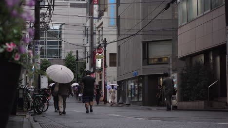 Pedestrians-on-a-typical-Tokyo-city-street-walk-to-work-with-umbrellas-on-a-wet-and-grey-morning