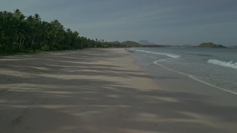 Low-forward-aerial-along-sand-beach-by-sea-and-forest-in-Philippines