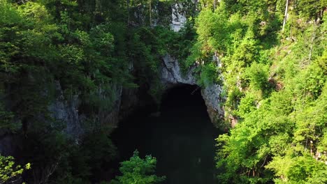 Aerial-shot-of-Cerknica-Cave,-Slovenia,-with-a-river-flowing-in,-surrounded-by-a-forest