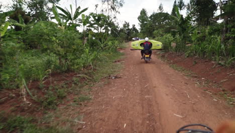 Local-paddlers-driving-their-boats-with-motorcycles-on-a-dirt-road-through-through-wilderness,-Uganda