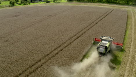 Static-drone-shoot-of-end-of-a-field-as-harvesting-combine-gathers-wheat--grain-leaving-strong-dust-trace-and-particles-in-the-air