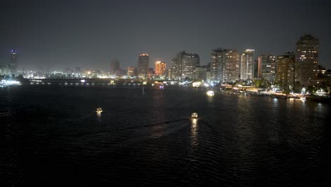 Boats-on-the-Nile-River-at-nighttime-with-the-Cairo,-Egypt-city-skyline-in-the-background