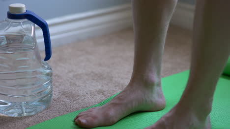 Close-up-shot-of-an-at-home-work-out-plus-a-green-yoga-mat,-yoga-mat-strap,-and-water-bottle