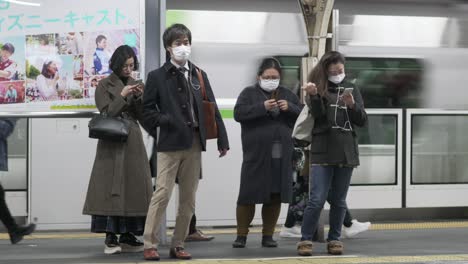 People-on-train-station-platform-in-Tokyo,-Japan,-wearing-surgical-face-masks-as-protection-against-pandemic-corona-virus-outbreak