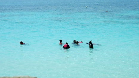 Tourists-Enjoy-Snorkeling-In-Bright-Blue-Sea-On-A-Hot-Weather---Travel-Destination-In-Perhentian-Islands,-Malaysia---wide-shot,-high-angle-1080p-60p