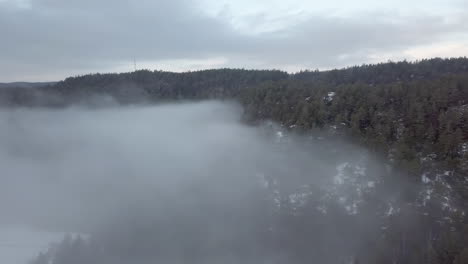 Aerial,-drone-shot,-panning-over-a-thick-fog-cloud,-surrounded-by-frosty-forest-and-hills,-on-a-foggy,-fall-morning,-in-Birkeland,-Aust-Agder,-South-Norway
