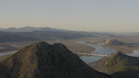 Vista-Panorámica-Del-Estuario-De-Un-Río-Con-Varias-Montañas-En-Forma-De-Pirámide-Con-Vegetación-Verde,-Al-Atardecer