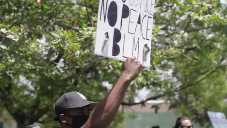 Black-Lives-Matter-Protestor-at-Rally-Holding-Sign,-No-Justice-No-Peace,-Slow-Motion-Pan