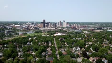 Wide-aerial-shot-slowly-panning-to-the-right-over-the-city-of-Saint-Paul,-Minnesota-on-the-horizon-by-the-Mississippi-river-surrounded-by-trees-and-houses-on-a-sunny-day
