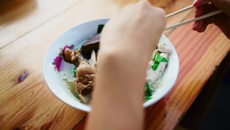 Woman's-hands-holding-chopsticks-and-putting-chicken-slices-and-noodles-to-a-Thai-spoon