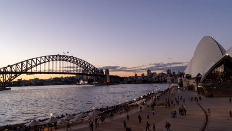 Timelapse-De-Día-A-Noche-De-Gente-Caminando-En-El-Paseo-Marítimo-Y-La-ópera-Con-Un-Puente-Al-Fondo-En-Sydney