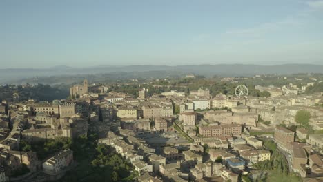 Drone-shot-of-Siena,-Italy,-starting-with-city-with-ferris-wheel-in-background,-pan-to-the-left-revealing-the-old-center-and-Piazza-del-Campo,-surrounding-towers-and-churches