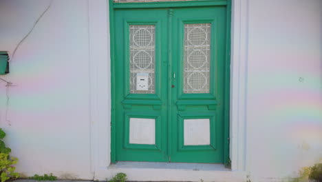 A-close-up-of-a-traditional-green-door-with-intricate-metalwork-on-a-white-wall-in-Lefkara,-Cyprus