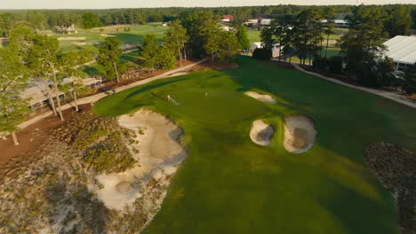 aerial-drone-shot-of-a-greenskeeper-watering-the-green-on-a-golf-hole-during-sunrise