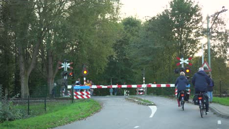 Cyclists-waiting-at-level-crossing-for-train-in-urban-park-suburb