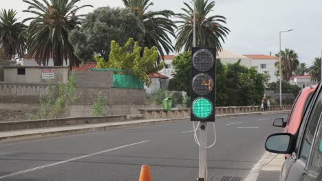 Temporary-traffic-light-with-timer-changes-colors-from-red,-amber-to-green-by-asphalt-road-with-car-driving-by-over-bridge-in-tropical-Porto-Santo-downtown-city-center,-Portugal,-static-close-up