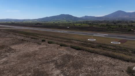 Airfield-airplane-takeoff-on-a-mexican-airport,-drone-shot,-mountains-backgraound