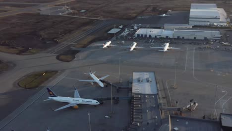 Boeing-airplanes-parked-at-gates-of-Iceland-airport-terminal-during-dusk,-aerial