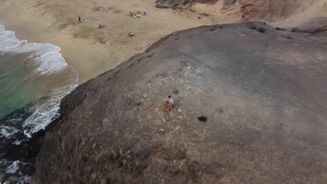 Rotating-aerial-drone-clip-of-a-guy-standing-on-a-mountain-close-to-the-sea-at-sunset