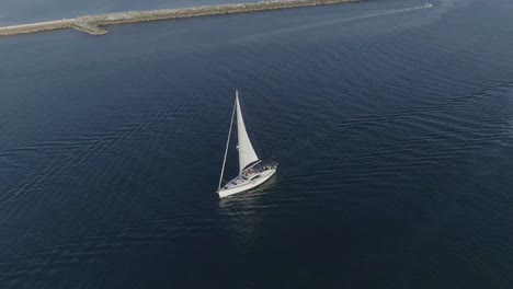 Aerial-shot-of-a-white-sailboat-passing-by-heading-into-the-Newport-Bay-in-Newport-Beach,-California