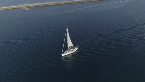 Toma-Aérea-De-Un-Velero-Blanco-Pasando-Por-La-Bahía-De-Newport-En-Newport-Beach,-California