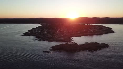 Aerial-drone-video-of-the-ocean-coastline-and-lighthouse-at-sunset-at-Nubble-Lighthouse-near-Cape-Neddick-and-York-Beach,-Maine,-United-States-of-America