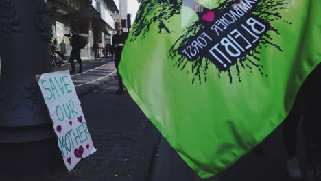 Ein-Schild-Mit-Der-Aufschrift-„Rettet-Unsere-Mutter“-Lehnt-An-Einer-Straßenlaterne,-Während-Klimaaktivisten-Vorbeimarschieren,-Um-Gegen-Die-Globale-Erwärmung-Zu-Protestieren