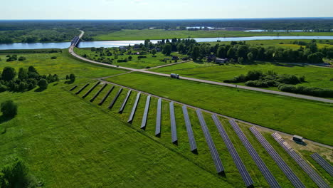 Solar-panel-farm-built-near-countryside-road-with-bridge-over-vast-river,-aerial-view