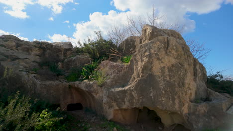 A-large-rock-formation-with-greenery-at-the-Tombs-of-the-Kings-in-Pafos,-Cyprus,-under-a-partly-cloudy-sky