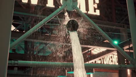 A-bucket-waterfall-in-a-factory-making-shiny-splashes-by-the-lights-on-the-manufacturing-equipment,-Slow-mo