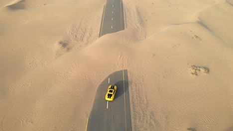 Revealing-aerial-drone-shot-of-a-Chevrolet-Camaro-in-the-middle-of-abandoned-desert-roads-covered-with-sand-in-Dubai,-UAE