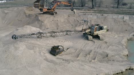 Aerial-flyby-shot-of-abandoned-heavy-machines-on-the-bank-of-a-lake-on-a-bright-day