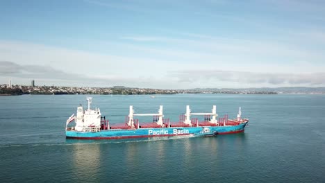 Large-cargo-ship-aerial-revealing-pan-at-high-angle,-with-west-Auckland-as-background