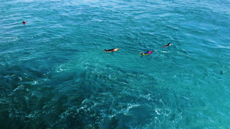 Drone-flying-towards-four-surfers-thare-are-floating-on-a-clear-blue-green-ocean