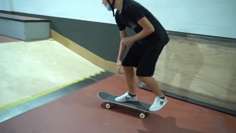 Kleiner-Junge-Mit-Maske-Macht-360-Skateboardtrick-Und-Grindet-Auf-Der-Schiene-Im-Indoor-Skatepark