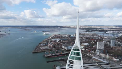 Close-fly-by-Spinnaket-Tower-Gun-Wharf-Quays-with-views-across-inner-Harbour,Portsmouth,HMS-Warrior-and-naval-dockyards-with-ferries-passing