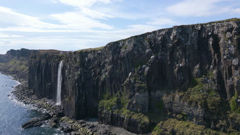 Kilt-Rock-Waterfall-cascading-off-cliffs-into-the-sea-under-a-bright-blue-sky-in-Isle-of-Skye,-Scotland
