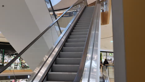 Moving-escalator-with-glass-sides-and-metal-steps-in-the-mall