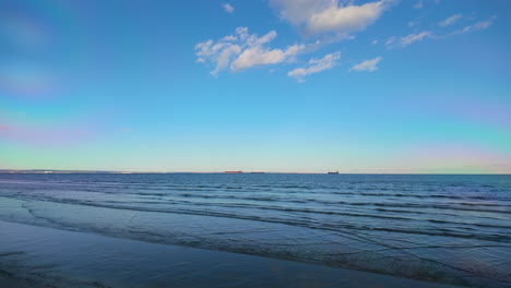 Eine-Ruhige-Strandszene-Mit-Sanften-Wellen,-Die-Unter-Einem-Klaren-Blauen-Himmel-Ans-Ufer-Plätschern