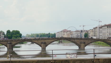 Historische-Brücke-überspannt-Einen-Ruhigen-Fluss-Mit-Einer-Stadtlandschaft-Und-Einem-Riesenrad-Im-Hintergrund