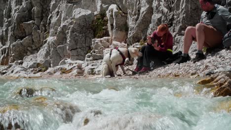Couple-with-dog-take-a-brake-from-hiking-next-to-a-stream-in-the-german-alps